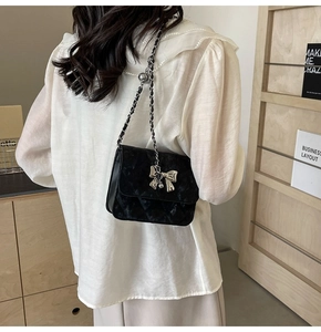 Detail of black velvet crossbody bag featuring silver bow charm and chain strap