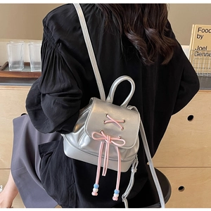 Close-up of silver PU leather mini backpack with pink lace-up bow and blue beaded details