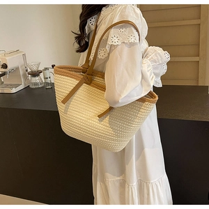 Straw tote bag with brown leather handles shown on shoulder of a model in white dress
