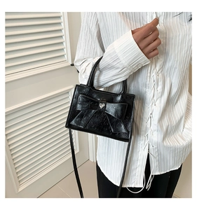 Vue détaillée du mini sac noir en cuir verni avec grand nœud et détail cœur argenté