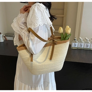 Detail of a large woven straw tote bag with brown straps and yellow tulips