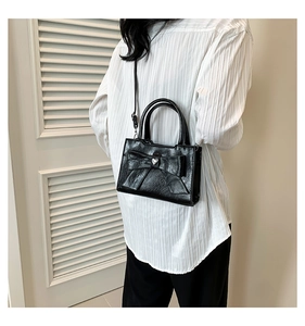 Modèle portant un sac bandoulière en PU brillant noir avec nœud et détail cœur argenté