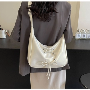 Rear view of cream PU leather hobo bag with bow details on a model in a minimalist setting