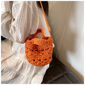 Detail of a vibrant orange hand-woven knit bucket bag paired with a white summer dress