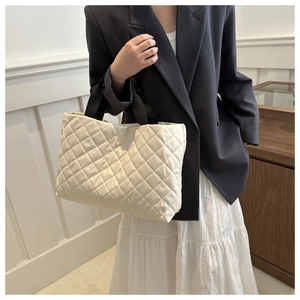 Gros plan d'un sac cabas matelassé beige avec anses noires porté par un mannequin
