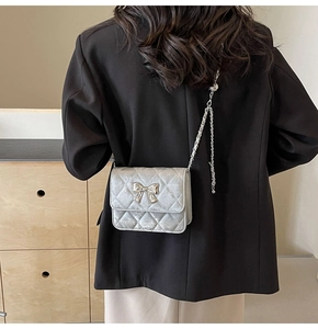 Silver quilted PU leather shoulder bag with a metallic bow detail worn on a black blazer