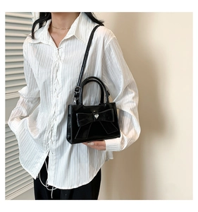Détail du sac bandoulière en similicuir noir brillant avec grand nœud et boucle cœur