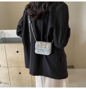 Silver quilted mini crossbody bag with a metallic bow detail worn over a shoulder