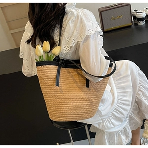 Detail of large woven straw tote bag featuring black leather trim and long shoulder straps