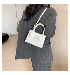 Gros plan d'un sac à bandoulière en cuir PU blanc avec un grand nœud et boucle en métal cœur