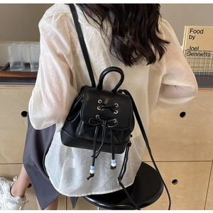 Detail of black PU leather mini backpack featuring drawstring bow and bead accents