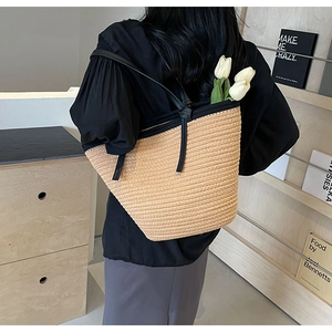 Detailed close-up of large straw tote bag with black contrast trim worn by model