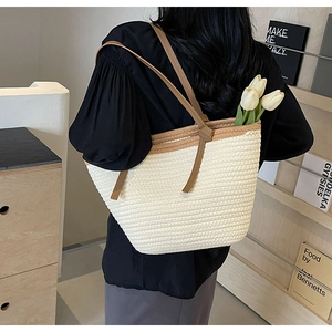 Detail of a large woven straw tote bag with brown leather straps shown in a cozy home setting