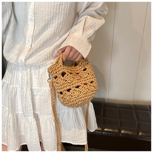 Close-up of beige woven knit crossbody bag paired with a white pleated dress in a chic setting