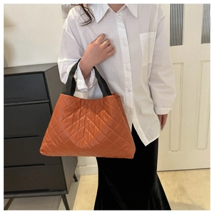 Détail du sac cabas matelassé orange avec anses en tissu noir porté par un mannequin