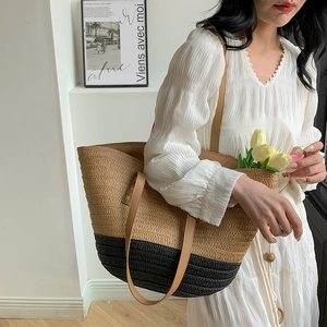 Detail view of woven straw tote bag featuring bicolor contrast stitching and faux leather handles