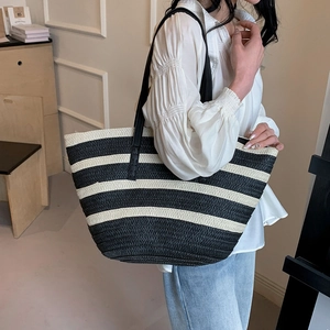 Close-up of woven straw tote bag with black and white stripes and leather straps