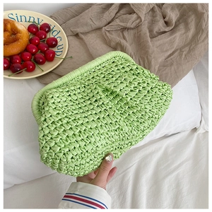 Detail view of a green hand-woven straw clutch bag on a bed with breakfast props