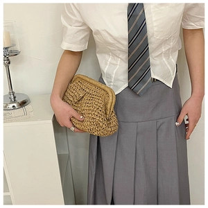 Handwoven straw clutch bag with natural texture shown held against a stylish outfit