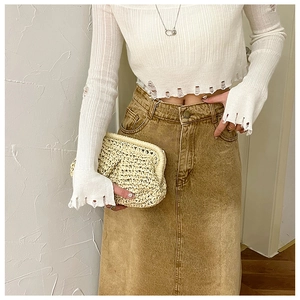 Detailed view of the woven texture on a minimalist cream straw clutch bag held by model