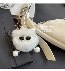 Close-up of fluffy white monster plush keychain with sunglasses on a minimalist handbag