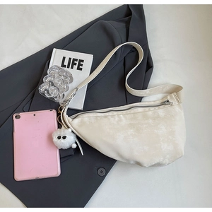 Macro shot of cream hobo bag with plush charm on a desktop with a grey suit and a book