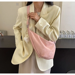 Pink crescent crossbody bag with plush charm and wide strap on yellow blazer