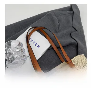 Close-up of woven straw tote bag with brown leather handles and metal rivet details