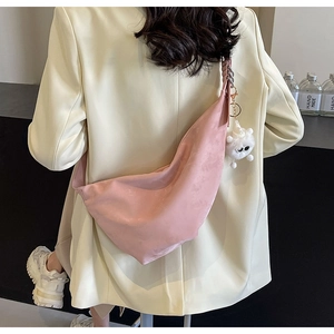 Pink crescent crossbody bag with plush monster charm worn by a model in a cream blazer