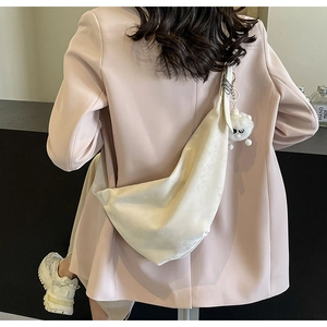 Detail of a creamy white crescent bag with a soft pleated texture and a cute plush charm