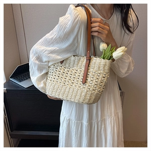 Detail of hand-woven straw tote bag with hollow pattern and brown leather straps