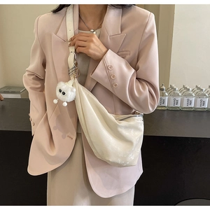Detail of a large beige crescent bag with soft texture and a plush mascot charm