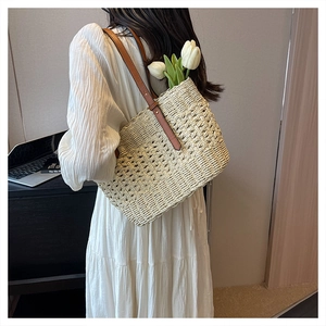 Detail of woven straw beach bag with brown leather strap worn by a woman in white dress