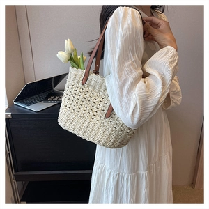 Detail of hand-woven straw tote bag with brown leather straps on a white dress