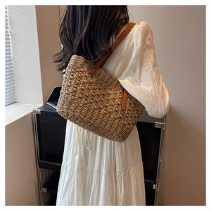 Detail of a minimalist straw tote bag with brown leather straps worn by a model