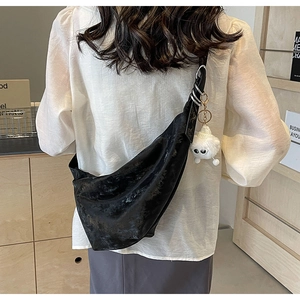 Detail of black wrinkled crescent bag with glossy PU leather and white plush charm