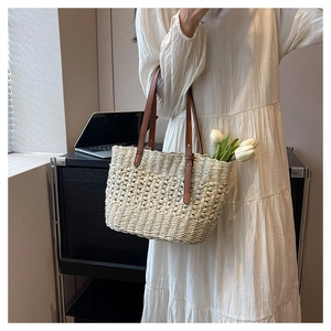 Close-up of woven paper straw texture and brown leather straps on a beige beach tote bag