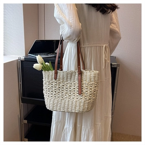 Close-up of woven straw tote bag with brown leather handles and hollowed-out flower patterns