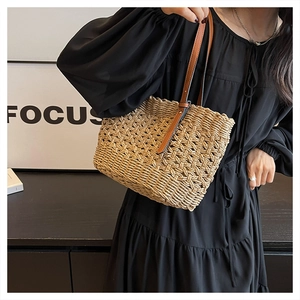 Detail of hollow woven straw tote bag featuring contrast brown faux leather shoulder straps