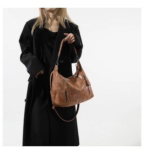 Close-up of vintage brown shoulder bag featuring dual zippers and pleated faux leather