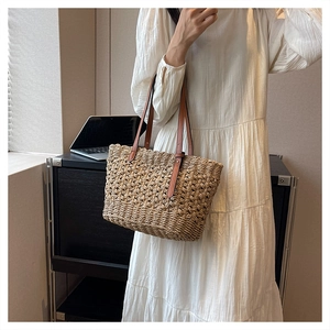 Fashionable woven beach bag with brown leather handles worn by a model in a white dress