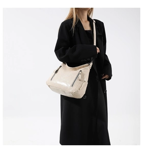 Chic cream leather shoulder bag with dual silver zippers styled on a black coat