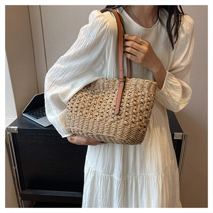 Detailed view of woven straw tote bag texture and slim brown leather shoulder straps
