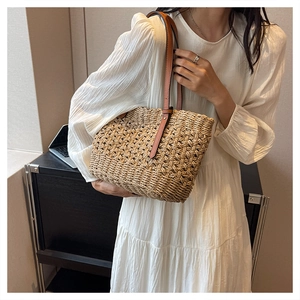 Detail of the woven paper straw texture and brown leather shoulder straps on a beige tote