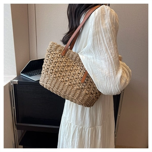 Close-up of woven paper rope straw tote bag with brown leather strap and cross texture