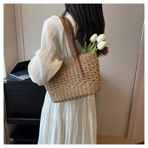 Detail of woven straw shoulder bag with brown leather straps and tulip decorative accent