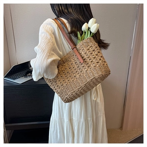 Detail of the woven texture and brown leather straps on this beige straw tote bag
