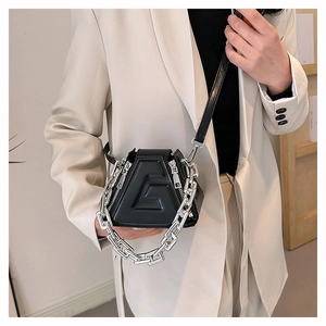 Detail of a black geometric mini crossbody bag featuring a 3D embossed G logo and thick silver chain