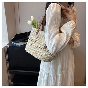 Detail of hollow woven straw tote bag featuring brown leather shoulder strap and interior flowers