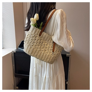 Detail of hollow woven straw tote bag with brown leather straps worn by model